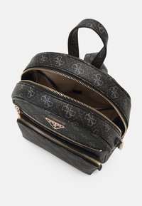 Mochila de imitación de cuero negra con herrajes plateados, patrón de logo, compartimentos con doble cremallera y un asa en la parte superior. Detalle de superficie texturizada visible.