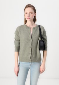 Light green wool cardigan with a round neck, button closure, and ribbed cuffs. Paired with light blue jeans and a black shoulder bag.