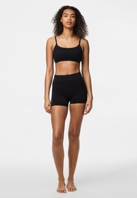 Cropped top nero con spalline sottili abbinato a pantaloni corti neri a vita alta. Entrambi i capi sono realizzati in tessuto liscio e elasticizzato.