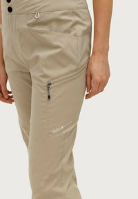 Beige outdoor broek van lichtgewicht stof met een ritszak, zijnaad en een logo op het been. Zachte textuur en een getailleerde pasvorm.