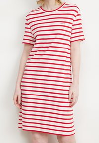 Femme portant une robe courte à manches courtes et à longueur genou avec des rayures horizontales rouges et blanches et un petit logo GANT sur la poitrine.
