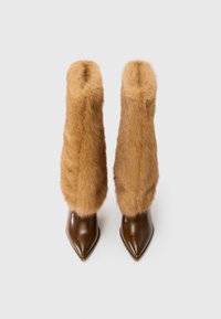 Botas de couro castanho de bico fino e salto alto, com cano alto de pele felpuda castanha clara cobrindo a área da perna.