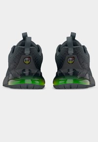 Ζευγάρι μαύρων και γκρι αθλητικών παπουτσιών Nike Air Max, εμφανιζόμενα από την πίσω πλευρά, με πράσινες σόλες αεροθαλάμων σε διαβάθμιση και λουράκια τραβήγματος, σε γκρι φόντο.