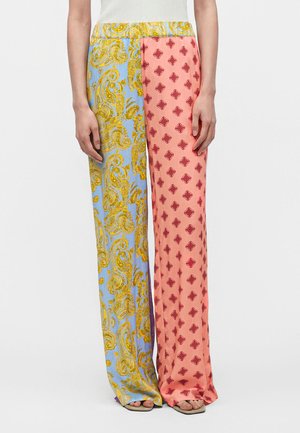Persoană purtând pantaloni largi; piciorul stâng este albastru cu model paisley galben, piciorul drept este roz cu modele mici roșii; vizibilă de la talie în jos.