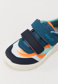 Sport shoe featuring blue and orange synthetic upper, velcro straps, and a textured sole. Design includes a light blue wave pattern.