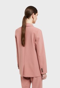 Ružový elegantný blejzer s jedným rozparkom vzadu, so štruktúrovanými plecami a gombíkovým detailom na manžetách. Hladká textúra látky.