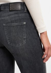 Dunkelgraue Denim-Jeans mit einer kleinen Gesäßtasche und einem Etikett am Bund, das wiederholten Text zeigt. Weiche Textur mit einer figurbetonten Passform.