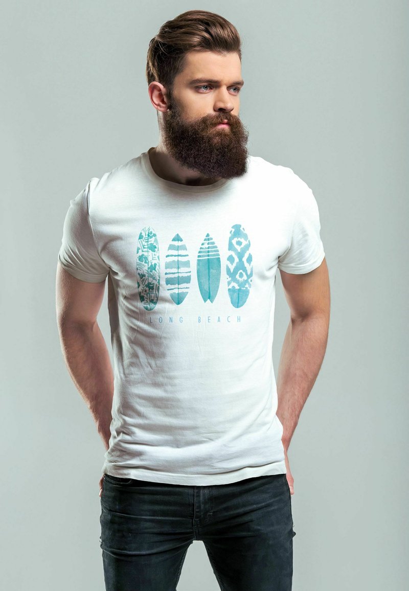 Weißes Baumwoll-T-Shirt mit einem blauen Grafikdesign von Surfboards in verschiedenen Mustern und dem Text "LONG BEACH" darunter. Getragen mit schwarzen Jeans.