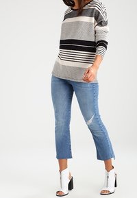 Czarny i kremowy sweter w paski, o luźnym kroju, zestawiony z jasnoniebieskimi jeansami o długości do kostek z postrzępionym wykończeniem i kieszeniami, białe botki za kostkę.