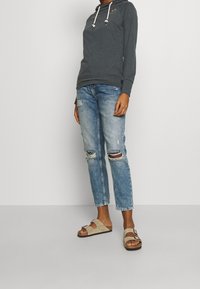 Grijze hoodie met trekkoord, blauwe distressed jeans met scheuren, en beige sandalen. Comfortabele, casual pasvorm met een minimalistisch ontwerp.