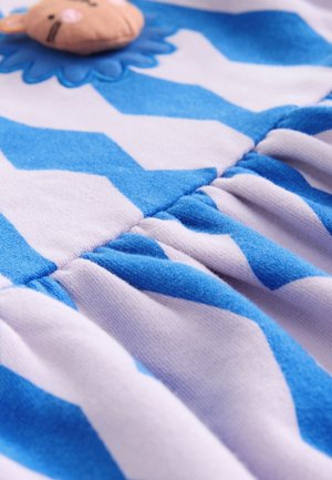 Tessuto blu e bianco con motivo a chevron, caratterizzato da un'applicazione di leone in rilievo su uno sfondo chiaro e dettagli in tessuto arricciato.