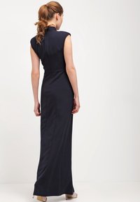 Mörkblå, ärmlös maxiklänning med hög krage, figursydd design och slät yta. Har en lång silhuett och ryggsömmar.
