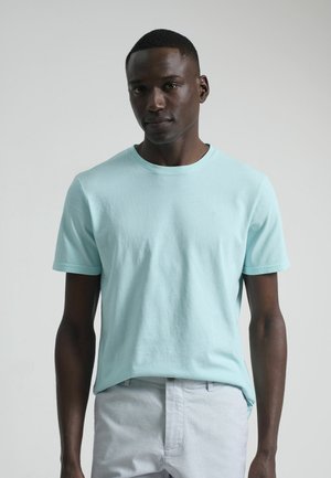 Camiseta de algodón azul claro con cuello redondo, mangas cortas y un sutil detalle de logo en el pecho. Textura suave, corte relajado.