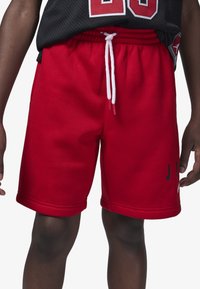 Pantalones cortos deportivos rojos hechos de tela suave, con una cinturilla elástica con cordones blancos y letras negras impresas en un costado.