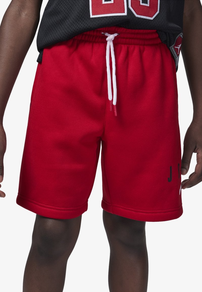 Pantalones cortos deportivos rojos hechos de tela suave, con una cinturilla elástica con cordones blancos y letras negras impresas en un costado.