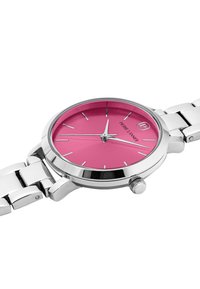 Reloj de acero inoxidable con una esfera redonda rosa, marcadores de horas plateados y pulsera de metal en tono plateado. Incluye una corona lateral para ajustes.