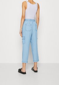 Jasnoniebieskie spodnie dresowe typu cargo z elastycznym pasem, dwiema kieszeniami z tyłu oraz skróconą długością. Połączone z czarnymi butami wsuwanymi.