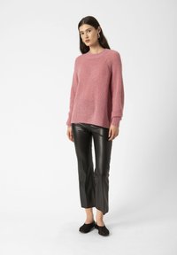 Pulover tricotat roz cu un finisaj texturat și mansete cu dungi, asociat cu pantaloni negri din piele ecologică și pantofi negri tip slip-on.