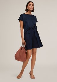 Top blu navy a maniche corte con dettaglio a fiocco, abbinato a pantaloni corti blu navy su misura e a una borsa testurizzata color rosa. Sandali nudi con cinturini completano il look.