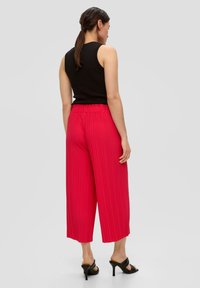 Rode geplooide wijde broek met elastische tailleband, gecombineerd met een zwart mouwloos topje en zwarte sleehak sandalen.