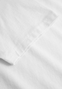 Țesătură de bumbac albă cu o textură netedă. Prezintă o margine pliată cu coasere curate, evidențiind un design curat și minimalist.