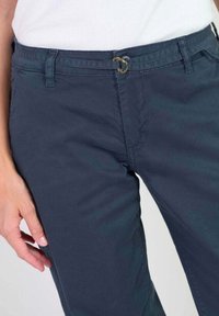 Marineblauwe katoenen broek met een comfortabele pasvorm, voorzien van een tailleband met lussen en goudkleurige hardware details op de tailleband. Gladde textuur.