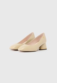 Pair of beige leather low block heel shoes with rounded toes and gold trim on heels on white background.