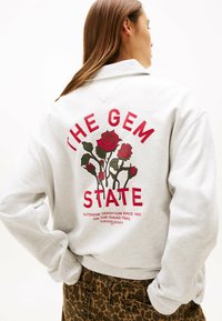 Grauer Sweater mit Rundhalsausschnitt, bedruckt mit rot-grüner Rosengrafik und dem Text "THE GEM STATE" auf der Rückseite. Weicher Stoff und lockere Passform.