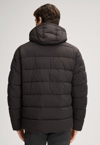 Giacca a vento nera con cappuccio, caratterizzata da un design trapuntato, texture liscia e polsini elasticizzati. Adatta per il freddo.