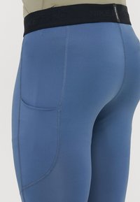 Μπλε κολάν Nike Pro με μαύρη ελαστική μέση. Διαθέτει πλαϊνή τσέπη και λείο, ελαστικό υλικό με επίπεδες ραφές.