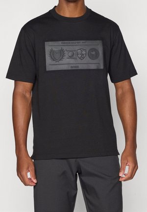 Man draagt een zwart T-shirt met reliëf golf-thema graphics en de tekst "Premium Golf Est. 1997" en "BOSS" op de borst.