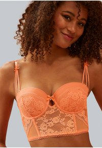 Reggiseno in pizzo pesche con pannelli in rete, dotato di ferretti, un dettaglio a fiocco centrale e spalline sottili regolabili. Accenti di motivo floreale in tutta la parte.