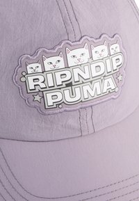 Lila pet met een textuur, voorzien van een rechthoekige patch met de tekst "RIPNDIP PUMA" en vier cartoonkatten.