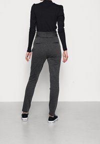 Pantalons taillés gris avec une taille haute et une coupe slim, dotés de deux poches arrière et d'une texture lisse, associés à des baskets noires.