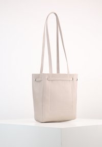 Jasnokremowa skórzana torba tote z dwiema długimi rączkami, prostymi liniami, prostokątnym kształtem i przednią kieszenią z minimalnymi detalami ściegów.