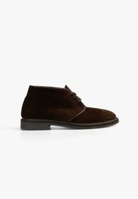 Botas de ante marrón hasta el tobillo con puntera redondeada, tacón bajo y diseño con cordones. Textura suave con suela negra contrastante y detalles de costura.