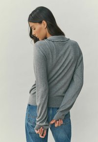 Gray sweater with a ruffled collar, long sleeves, and ribbed hem, paired with blue denim jeans featuring back pockets.