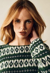 Stickad tröja med ett geometriskt mönster i grönt och vitt med inslag av grått. Urringningen är rund och texturen ser mysig och mjuk ut.