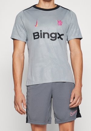 Mann trägt graues Fußballtrikot und Shorts mit pinken Nike-Logos und dem Sponsor BingX auf der Vorderseite des Trikots.