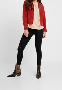 Röd mockajacka med dragkedja, beige oversized t-shirt, svarta ripped skinny jeans och bruna ankelboots med ormskinnspray.