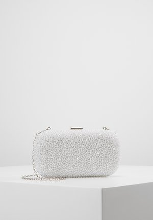 Pochette rectangulaire blanche recouverte de petites perles avec une chaîne argentée posée sur une surface blanche.