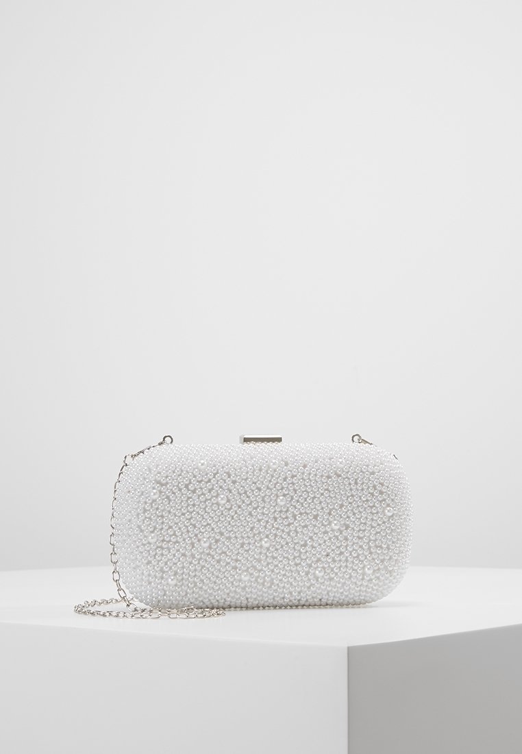 Pochette rectangulaire blanche recouverte de petites perles avec une chaîne argentée posée sur une surface blanche.