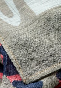 Lærredsstof, der viser en lys beige tekstur med en kontrasterende marineblå og lyserød mønstrede kant, med præcise syninger langs kanterne.