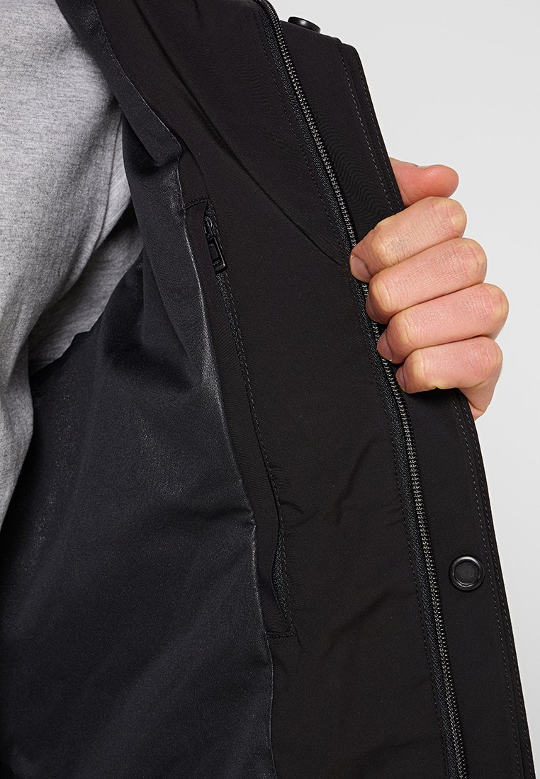 Schwarzes Jacket-Innenfutter mit glatter Textur, ausgestattet mit einer seitlichen Reißverschlusstasche und einer Nahaufnahme des Stofffutters. Hand sichtbar.