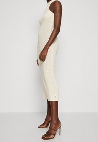 Robe midi en tricot crème avec un col montant, une texture côtelée et des fentes latérales. Associée à des sandales à talons hauts strappy marron.