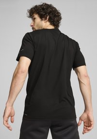 Camiseta deportiva de manga corta negra con una textura suave. Presenta un cuello redondo y un sutil logotipo en la manga. Diseño ajustado.
