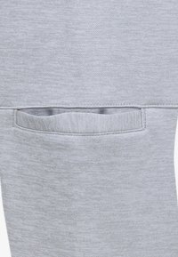 Material elastic de culoare gri deschis, cu un mic buzunar orizontal, cu o textură moale și margini fără cusături, conceput pentru utilizare practică.