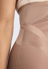 Beige formende plagg med glatt tekstur, som har gjennomsiktige seksjoner og buede sømmer, som fremhever en slank design. Stretch-materiale.