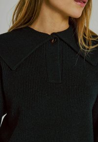 Schwarzer gestrickter Pullover mit einem Kragen, strukturiertem Stoff und einer Knopfleiste vorne.