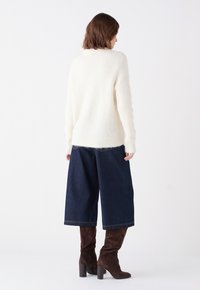 Pullover bianco fluffy, pantaloni di jeans a gamba larga blu scuro e stivali al ginocchio in suede marrone; texture morbida, vestibilità rilassata e polsini a costine.